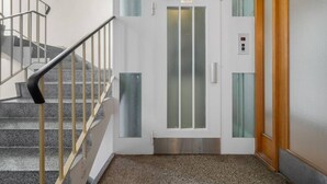 A modern elevator with a glass door, a metal handrail, and a control panel.
