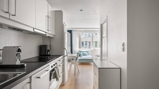 A narrow, modern kitchen with white cabinetry, a black countertop, and a coffee machine.