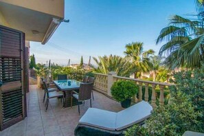 Een balkon met een tafel, stoelen, een kleine bloempot en een lounge stoel.