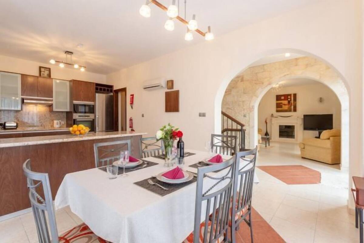 A modern kitchen with a dining area, a living room with a sofa, and an archway leading to another room.