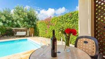 Un área junto a la piscina con una mesa, sillas, una botella y un jarrón con flores.