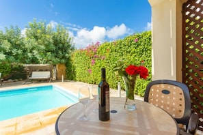 A poolside area with a table, chairs, a bottle, and a vase with flowers. - Villa Evelina (Neokhorio)