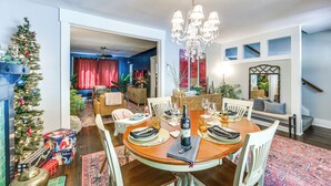 A dining area with a wooden table set for four, surrounded by white chairs. A chandelier hangs above the table, and a Christmas tree is visible in the background. - Easy Access to Pittsburgh: Urban Retreat w/ Deck (Pittsburgh)