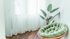 Een kamer met een groene fauteuil, een potplant en dunne gordijnen.