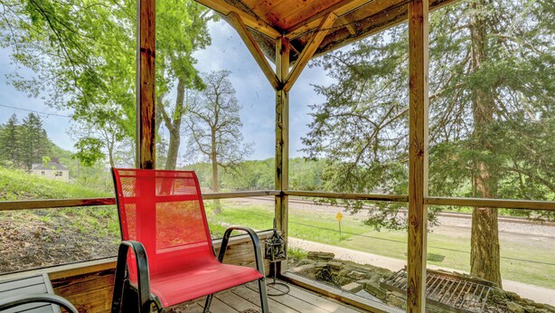 A covered porch with a red chair, wooden table, and a view of a road and trees.