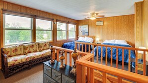 A bedroom with two beds, a wooden ceiling, and large windows.