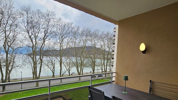 A balcony with a view of a lake, trees, and a distant building.