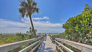 A wooden boardwalk leading to the beach with railings on both sides, surrounded by greenery and palm trees. - Golden Mile Escape for Extended Winter Stays (Myrtle Beach)