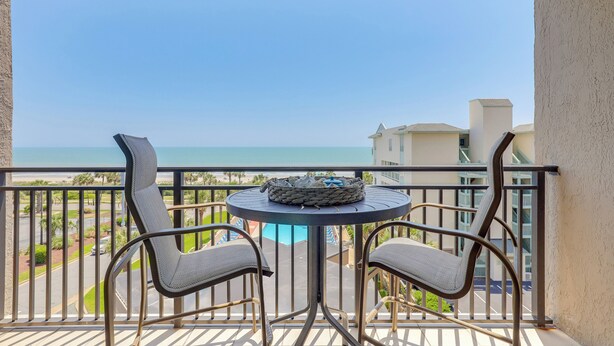 A balcony with two chairs and a table, overlooking a pool and a clear blue sky. - Golden Mile Escape for Extended Winter Stays (Myrtle Beach)
