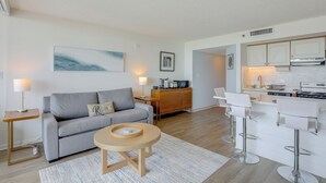 A modern living room with a grey sofa, a round coffee table, and a kitchen area with white bar stools. - Golden Mile Escape for Extended Winter Stays (Myrtle Beach)