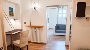 Una habitación con piso de madera, un escritorio con silla, un radiador, un sofá y un cuadro en la pared.