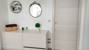 Un tocador blanco con espejo y repisas, una puerta de madera y una pequeña planta.