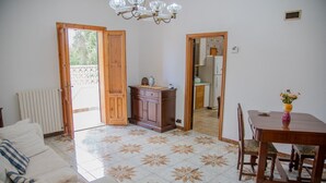 A living room with a sofa, a dining table with chairs, a wooden cabinet, and a kitchen visible through an open door. - Villa Ada - Leporano Marina (Leporano Marina)