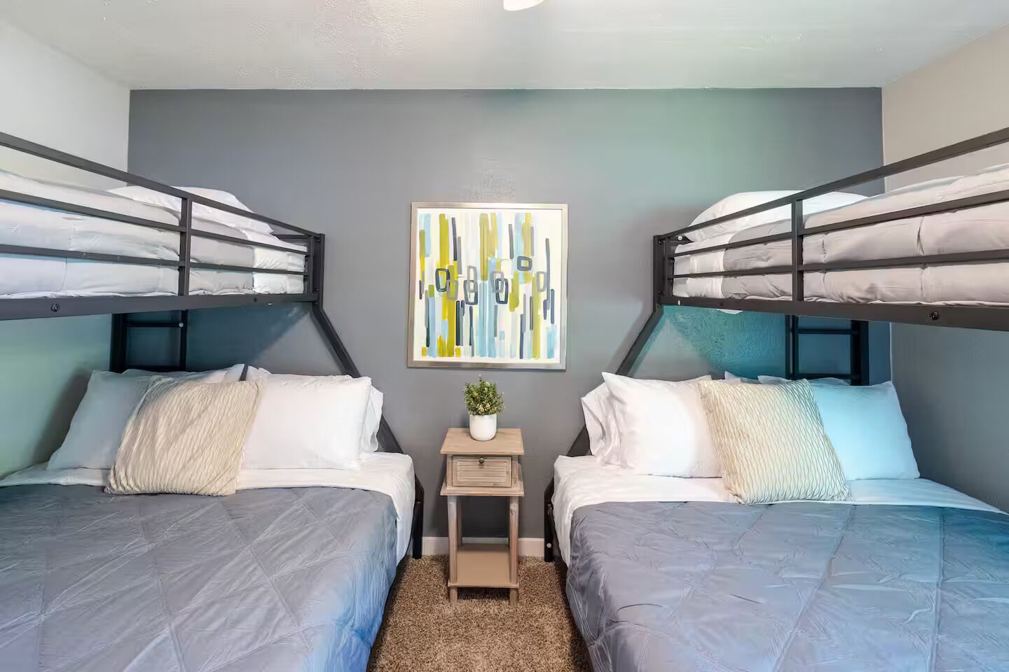 Een kamer met twee stapelbedden, een klein nachtkastje met een plant, en een abstract kunstwerk aan de muur.