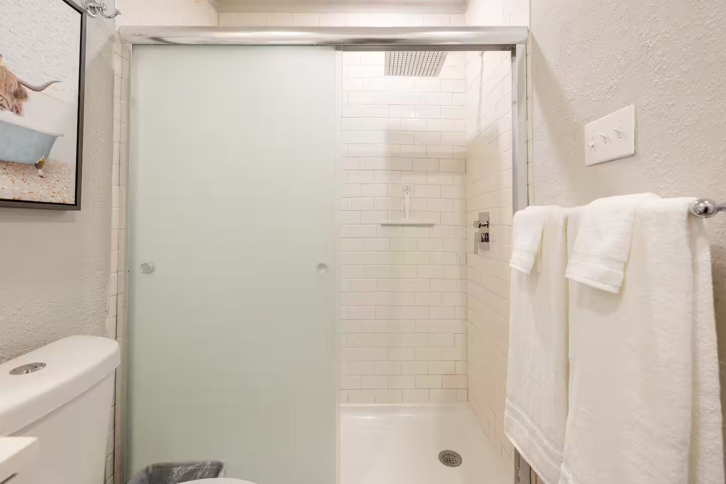 Ein Badezimmer mit Duschkabine aus Glas, weißen Fliesenwänden, einer Toilette und einem Handtuchhalter.