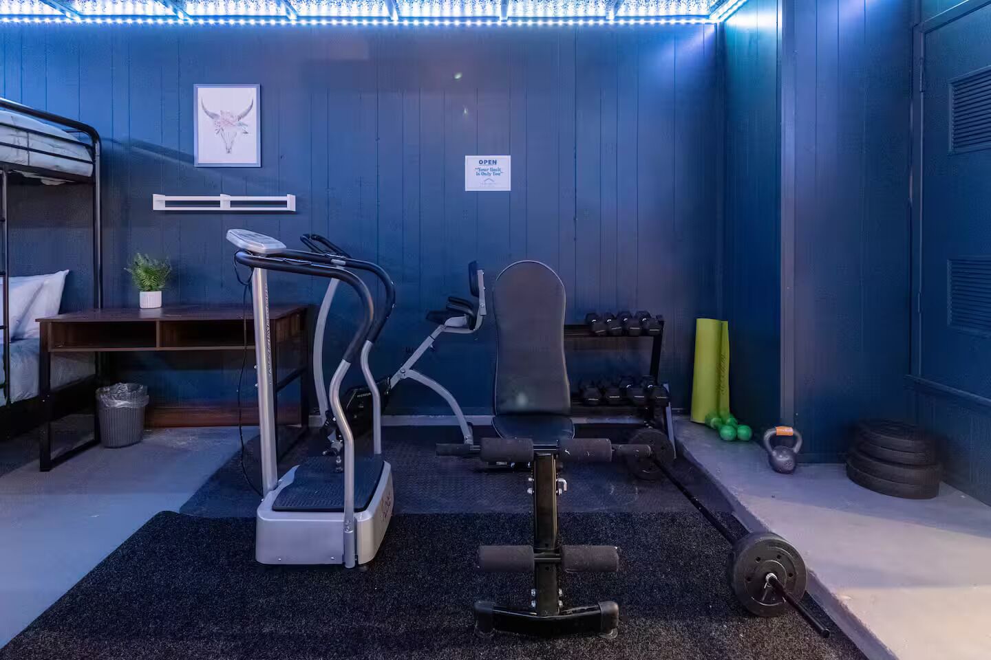 Une salle de sport compacte équipée de machines de cardio, d’haltères et d’un banc.