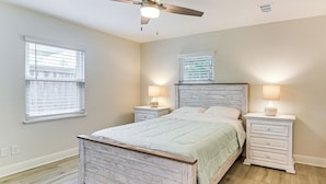 A bedroom with a wooden bed, two bedside tables with lamps, a ceiling fan, and a window with blinds. - Steps to Seawall: Fenced Family Home in Galveston! (Galveston)
