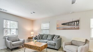 A living room with a grey sofa, a wooden coffee table, and a painting of a pier on the wall. - Steps to Seawall: Fenced Family Home in Galveston! (Galveston)