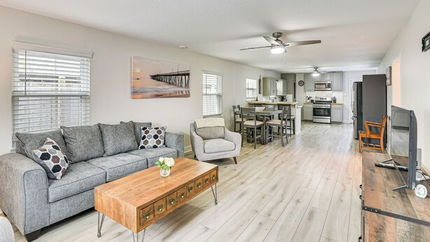 A spacious living area with a grey sofa, wooden coffee table, and a dining area with a table and chairs. - Steps to Seawall: Fenced Family Home in Galveston! (Galveston)
