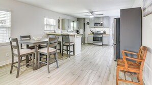 A modern kitchen with a dining area, featuring a central island, grey cabinets, and a microwave. - Steps to Seawall: Fenced Family Home in Galveston! (Galveston)