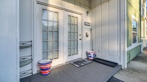 Un edificio blanco con dos puertas, un cartel de bienvenida y un cubo a rayas en el porche.