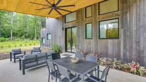 Eine Terrasse im Freien mit Holzboden, einem Tisch und Stühlen und Blick auf ein bewaldetes Gebiet.