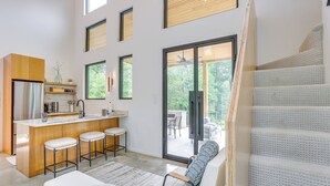 Eine moderne Küche mit einer zentralen Kochinsel, Barhocker und einem großen Schiebeglastür, die auf eine Terrasse im Freien führt.