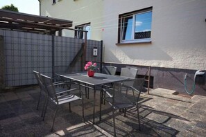 An outdoor patio with a table and chairs, a potted plant, and a view of a house. - Großzügiges Apartment Nahe Frankfurt (Muhlheim am Main)