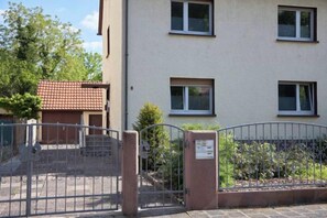 A building with a gated entrance, a small garden, and a red-tiled roof visible in the background. - Großzügiges Apartment Nahe Frankfurt (Muhlheim am Main)