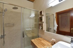 Un baño moderno con cabina de ducha de vidrio, tocador de madera y un espejo grande.