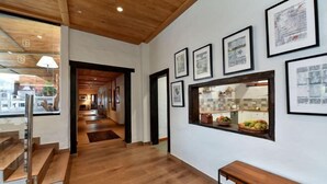 A hallway with wooden flooring, a bench, framed artwork on the wall, and a window with a view of a kitchen. - Finca la Casona de Abajo Arucas (Arucas)