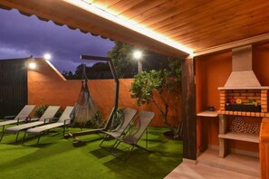 An outdoor patio with a brick oven, green artificial turf, and lounge chairs.