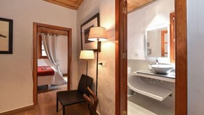 A room with a wooden ceiling, a chair, a lamp, a bed with a red cover, and a bathroom with a white sink and mirror. - Finca la Casona de Abajo Arucas (Arucas)