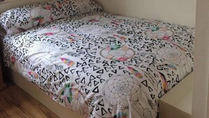 Ein kleines Zimmer mit einem Einzelbett, einer gestreiften Bettdecke, einem Holz-Kopfteil und einer schrägen Decke.