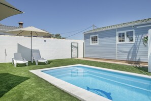 Un jardin avec une piscine, deux chaises longues et une maison à l’extérieur blanc.