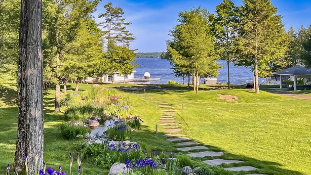 Ein Garten mit einem gepflasterten Weg, der zu einem Gazebo an einem See führt.