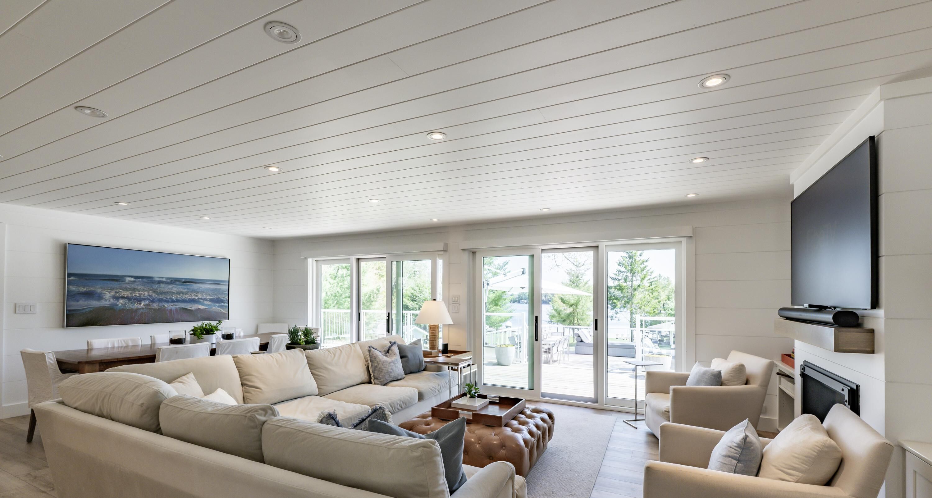 A spacious living room with a large sectional sofa, a flat-screen TV mounted on the wall, and a sliding glass door leading to an outdoor area.