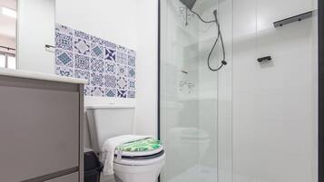Un baño con inodoro, cabina de ducha y pared con azulejos.