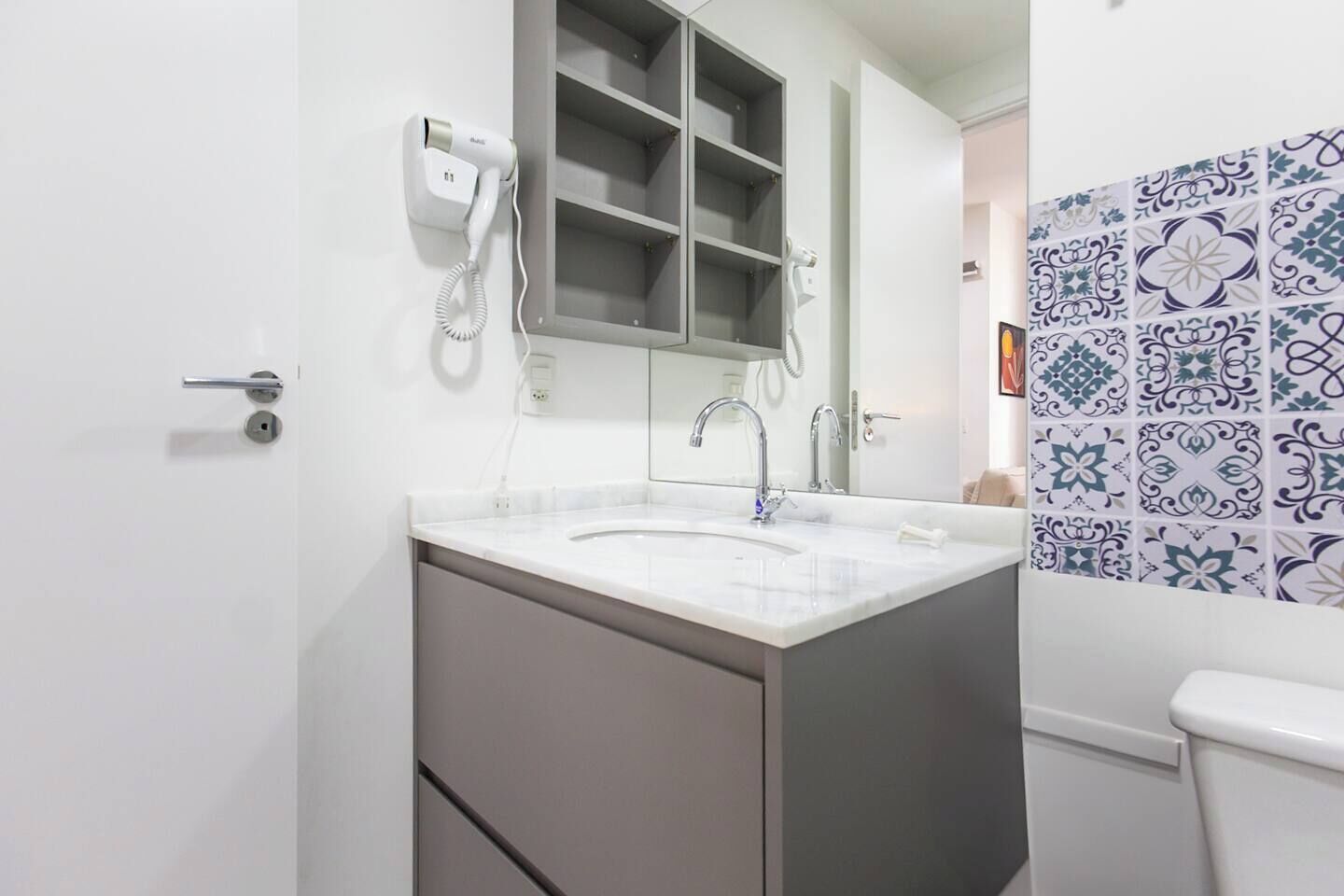 A bathroom with a white sink, a mirror, a hairdryer, and a toilet.