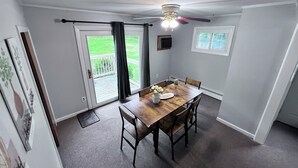 Un comedor con una mesa y sillas de madera, un ventilador de techo y vistas al exterior a través de una puerta corrediza de vidrio.