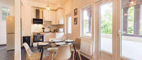 Una cocina moderna con armarios blancos, un microondas negro y un comedor con mesa y sillas de vidrio.
