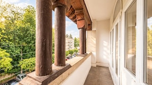 A balcony with wooden columns, a white wall, and a view of a building and trees.
