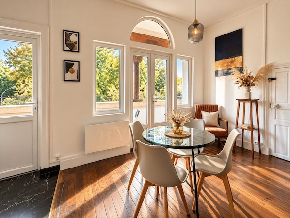 A dining area with a round glass table, white chairs, and a vase with dried flowers.