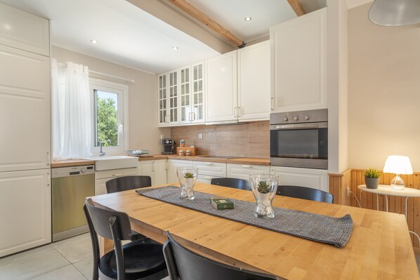 A modern kitchen with white cabinets, a wooden dining table, and a built-in oven.
