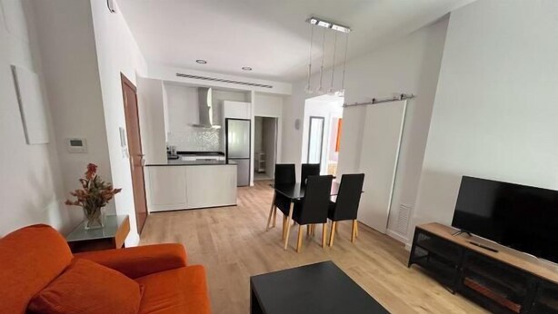 A modern living room with a sofa, a coffee table, a TV, and a dining area with chairs and a table. - Loreto N1 (Denia)