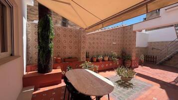Un patio exterior con mesa y sillas, plantas en macetas y una escalera.