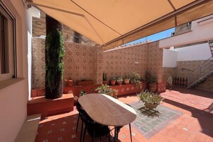 Un patio exterior con mesa y sillas, plantas en macetas y una escalera.