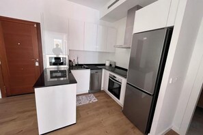 A compact kitchen with white cabinets, a black countertop, a stainless steel refrigerator, and a microwave. - Loreto N1 (Denia)
