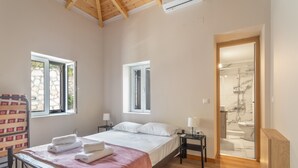 Une chambre à coucher avec un lit, des tables de chevet, un plancher en bois et une salle de bain visible à travers une porte ouverte.