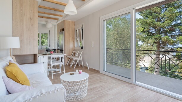 Un salon moderne avec un canapé, une table à manger et un balcon offrant une vue sur les arbres.